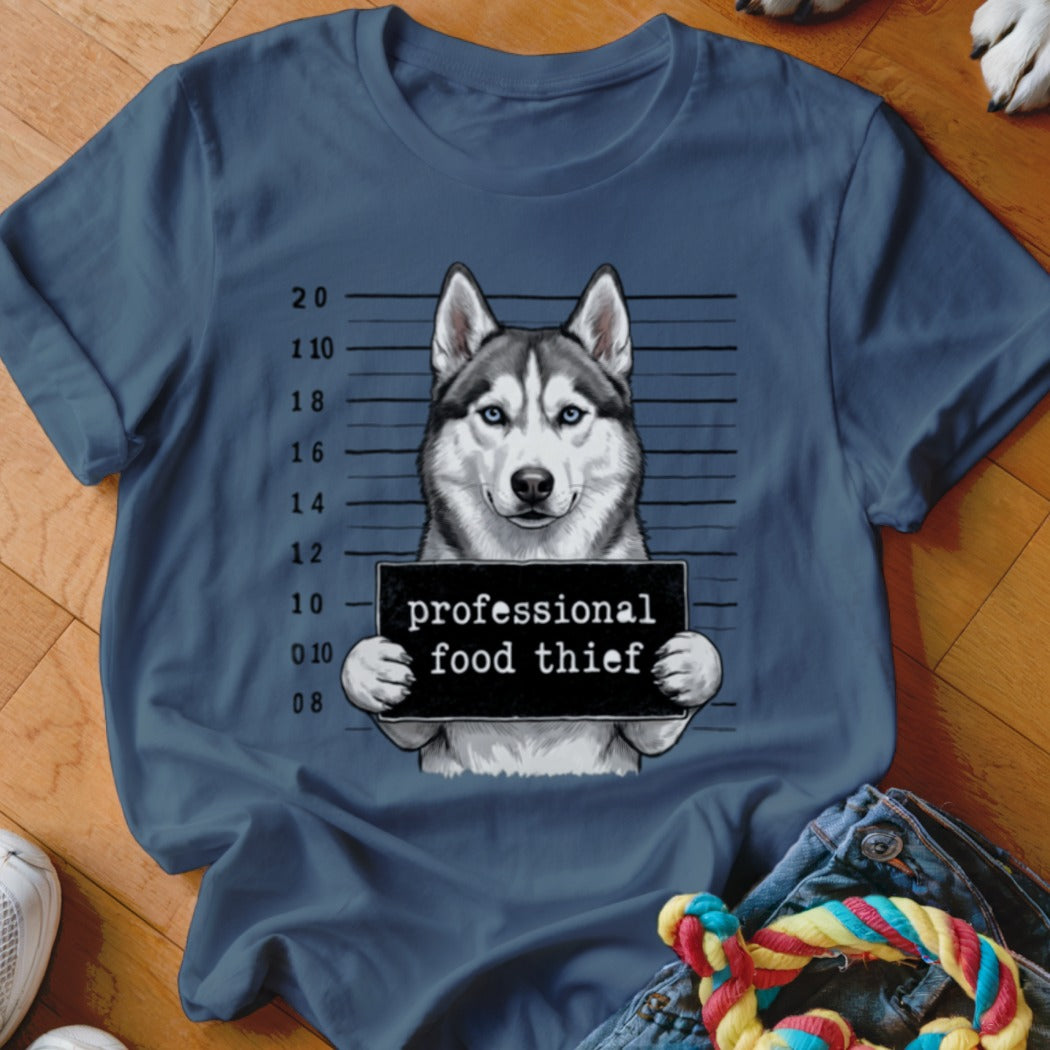 Husky dog holding a "professional food thief" sign with mugshot background.