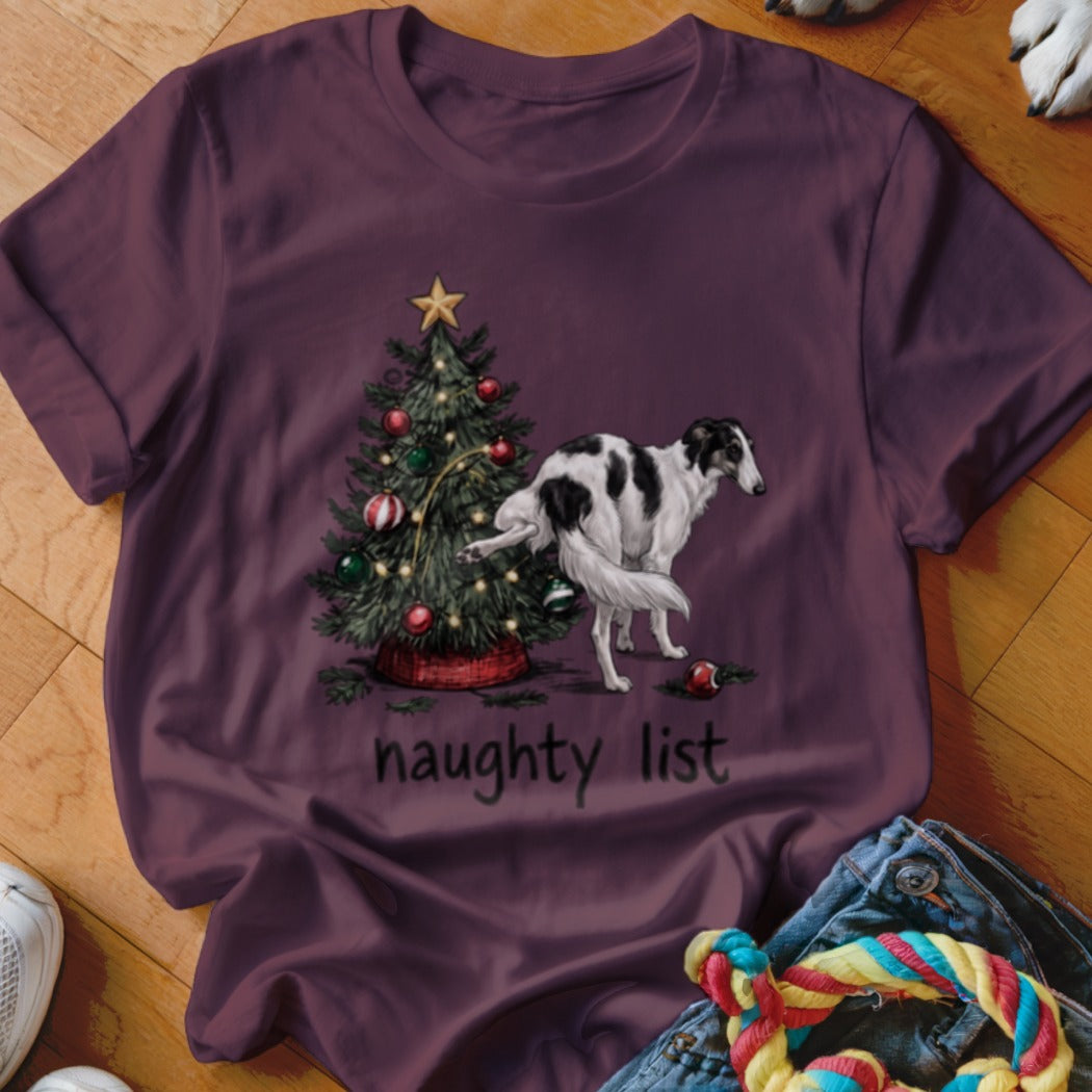 A maroon t-shirt with a graphic of a borzoi dog peeing on a Christmas tree, with the text "naughty list".