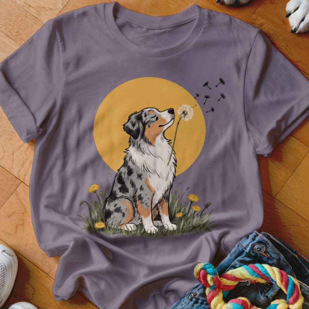 A purple t-shirt featuring an illustration of an Australian Shepherd blowing a dandelion seed head.