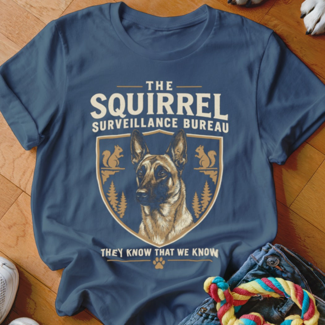 A dark blue t-shirt featuring a graphic of a German Shepherd inside a crest with squirrels and text reading The Squirrel Surveillance Bureau.
