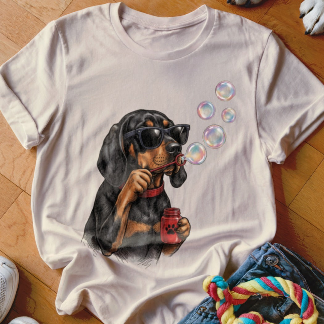 A light beige t-shirt with a graphic of a black and tan dog wearing sunglasses and blowing bubbles.