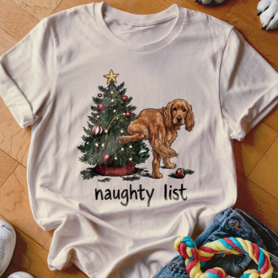 T-shirt graphic of a dog lifting its leg on a Christmas tree with "naughty list" text.