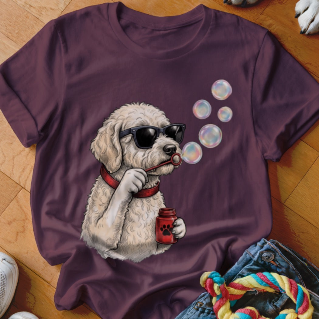 A dark purple t-shirt featuring an illustration of a fluffy white dog wearing sunglasses and blowing bubbles.