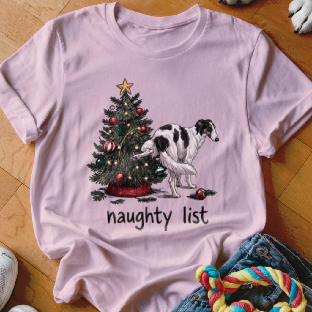 A pink t-shirt displays an illustrated graphic of a dog lifting its leg against a decorated Christmas tree, with the text "naughty list" underneath.