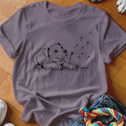 A purple crewneck t-shirt featuring a black line art graphic of a puppy looking at dandelion seeds.