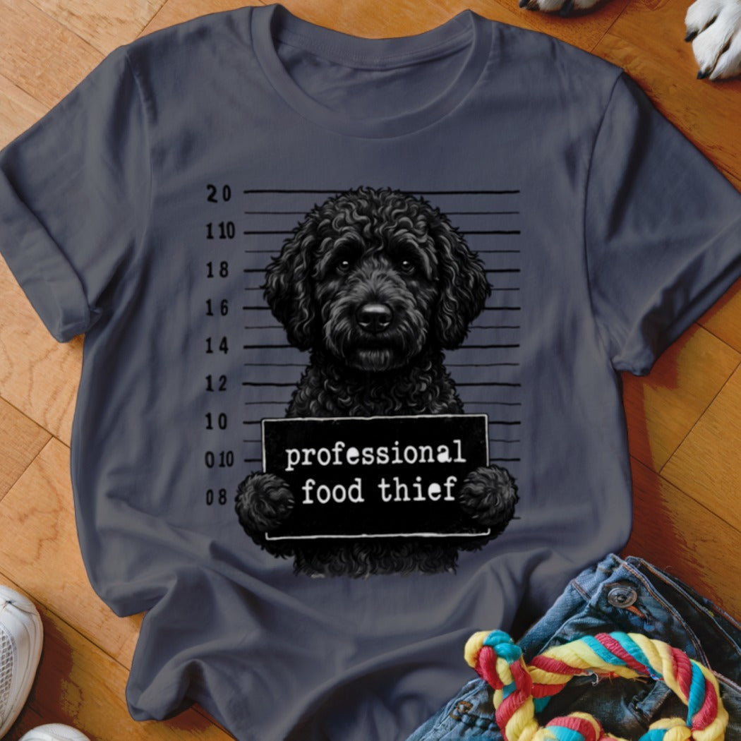 Black poodle mugshot with "professional food thief" sign on charcoal shirt.