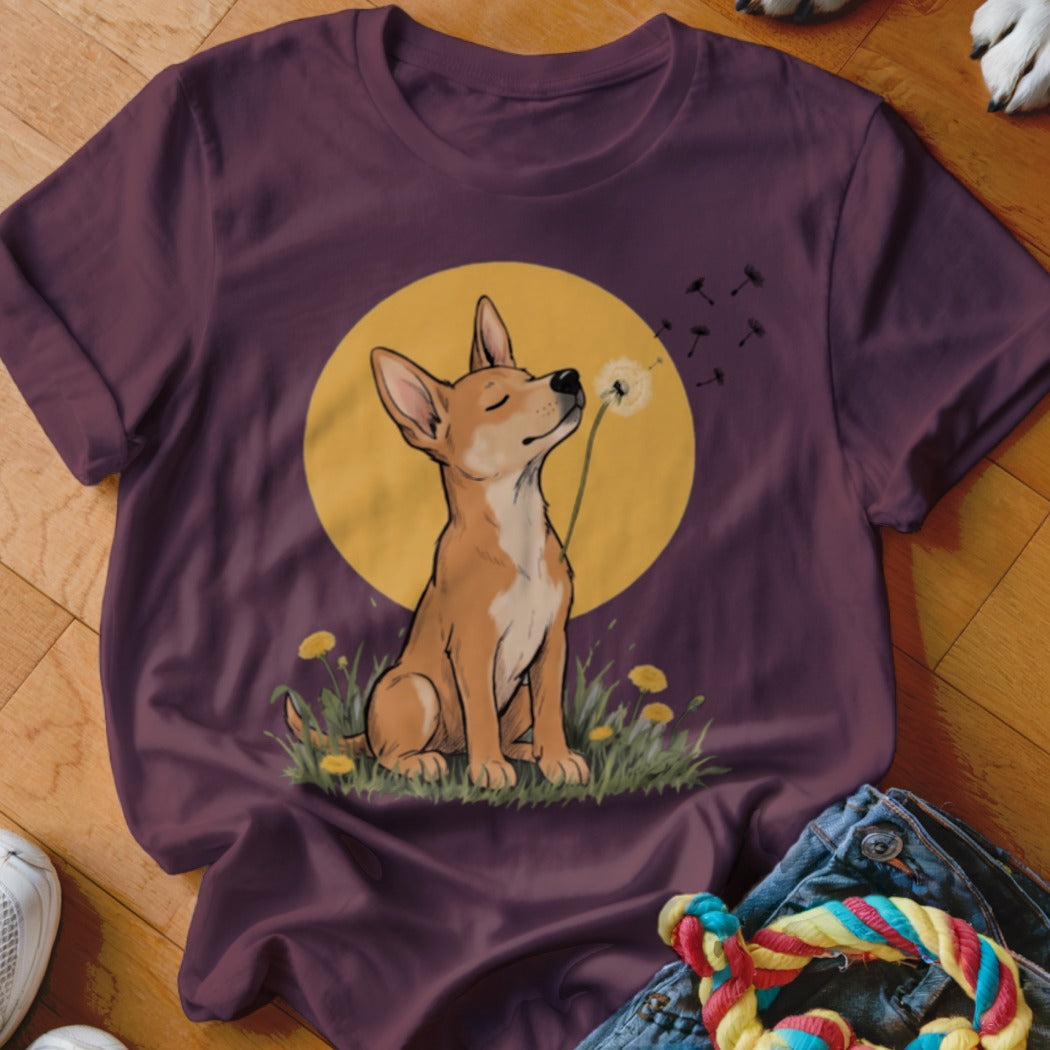 A dark purple t-shirt features a graphic of a brown dog blowing dandelion seeds against a yellow circle.