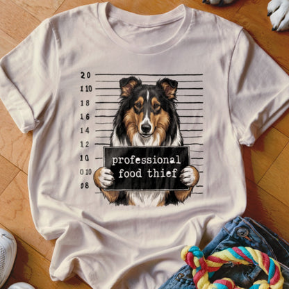 Sheltie dog mugshot with "professional food thief" sign on a t-shirt.