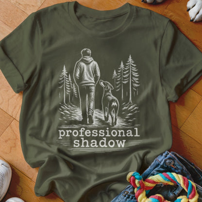 Olive green t-shirt with a sketch of a person and dog walking on a trail with trees, text reads "professional shadow".
