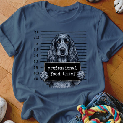 Dog mugshot with "professional food thief" sign on a blue t-shirt.