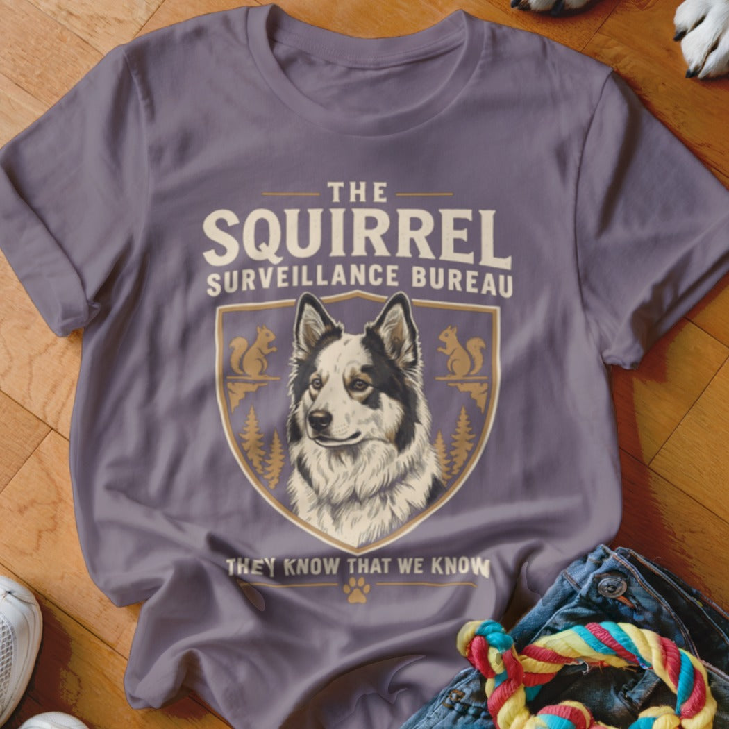 Purple t-shirt featuring a graphic of a dog, squirrels, and the text The Squirrel Surveillance Bureau.