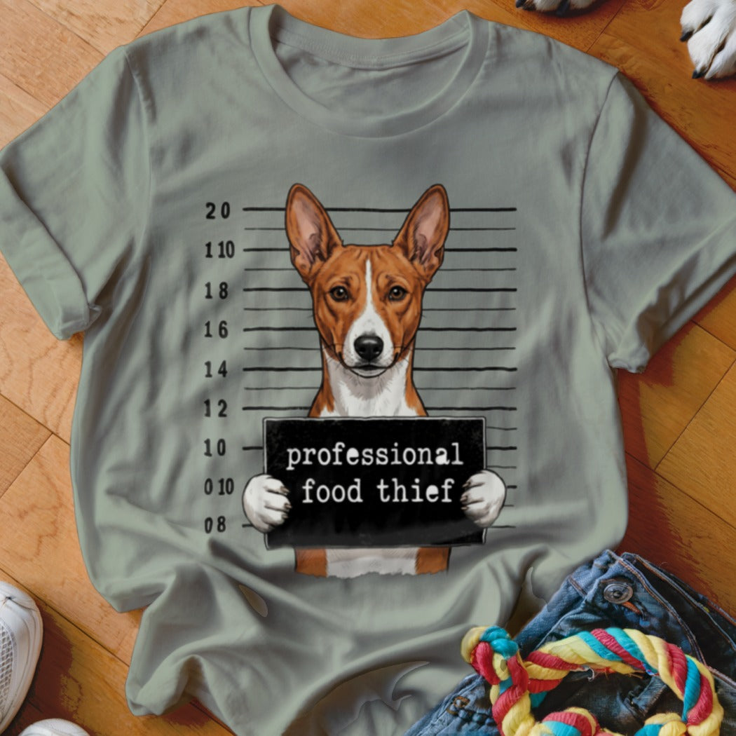 Basenji dog mugshot with "professional food thief" sign on a t-shirt.