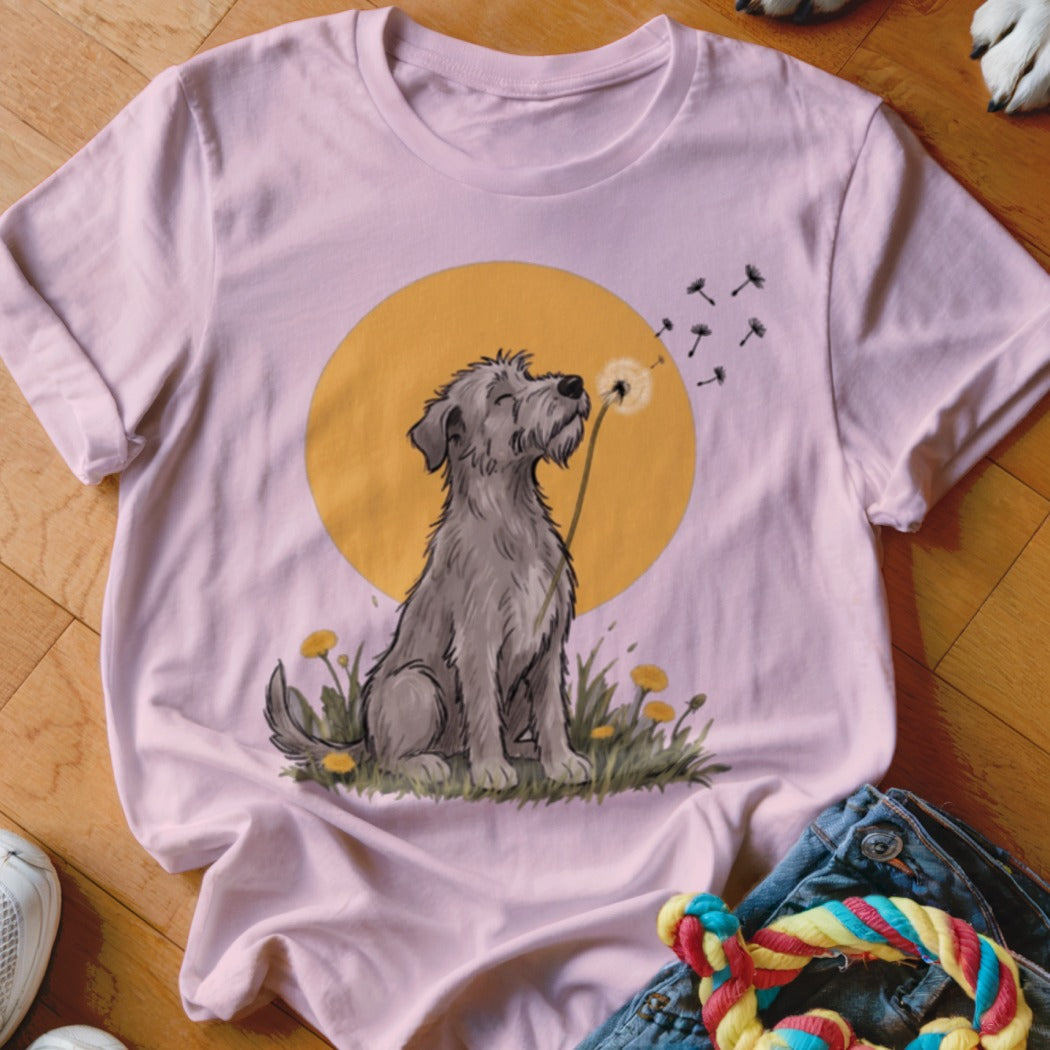 A light pink t-shirt featuring a graphic of a shaggy gray dog blowing dandelion seeds.