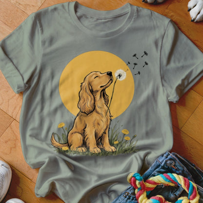 Sage green t-shirt featuring a graphic of a golden retriever blowing dandelion seeds against a yellow sun.