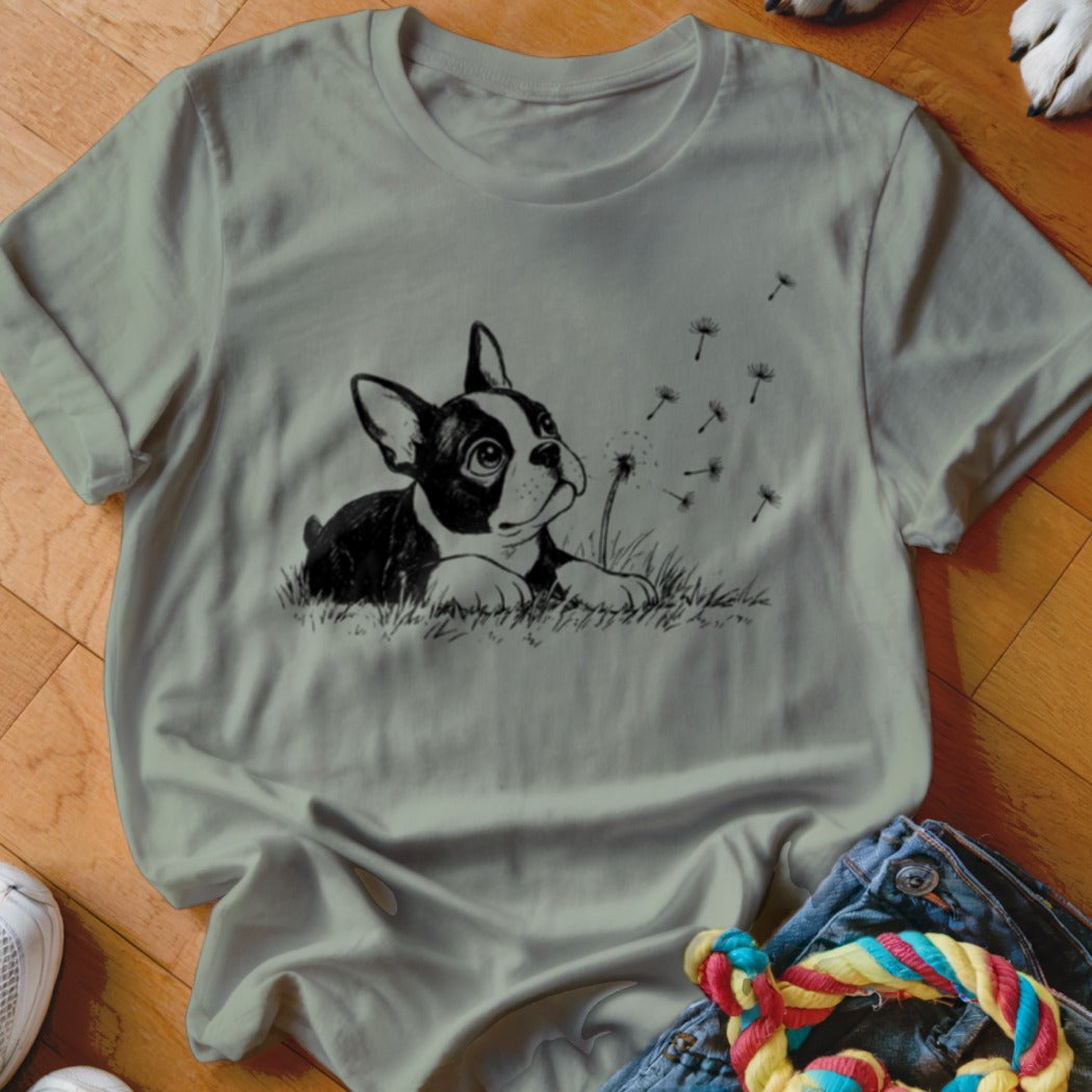 Sage green t-shirt featuring a black and white graphic of a puppy watching blowing dandelion seeds.