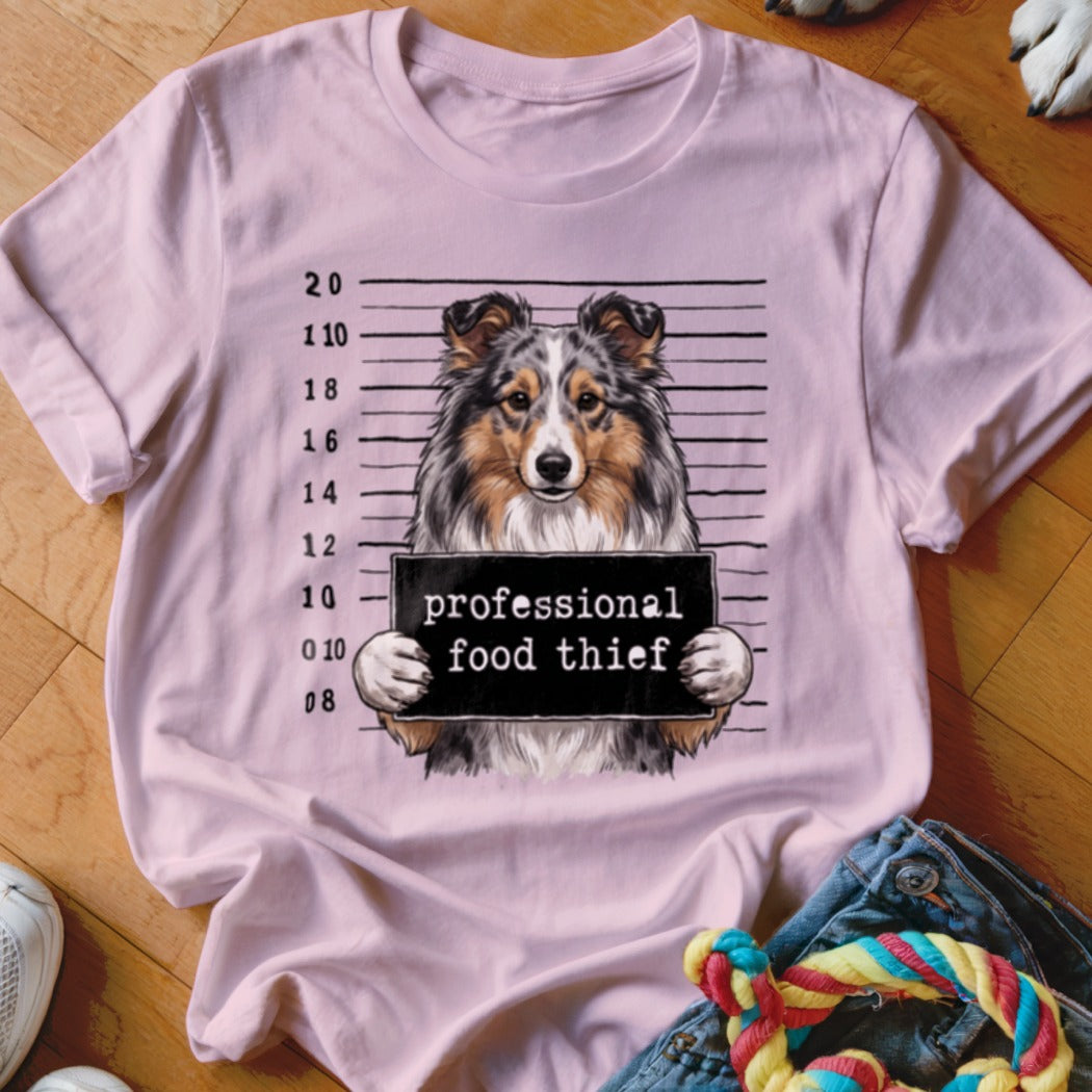 Light pink t-shirt with a dog in a mugshot holding a sign that says "professional food thief".
