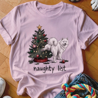 Light pink crewneck t-shirt featuring a cartoon of a white dog lifting its leg on a Christmas tree, with the text naughty list underneath.