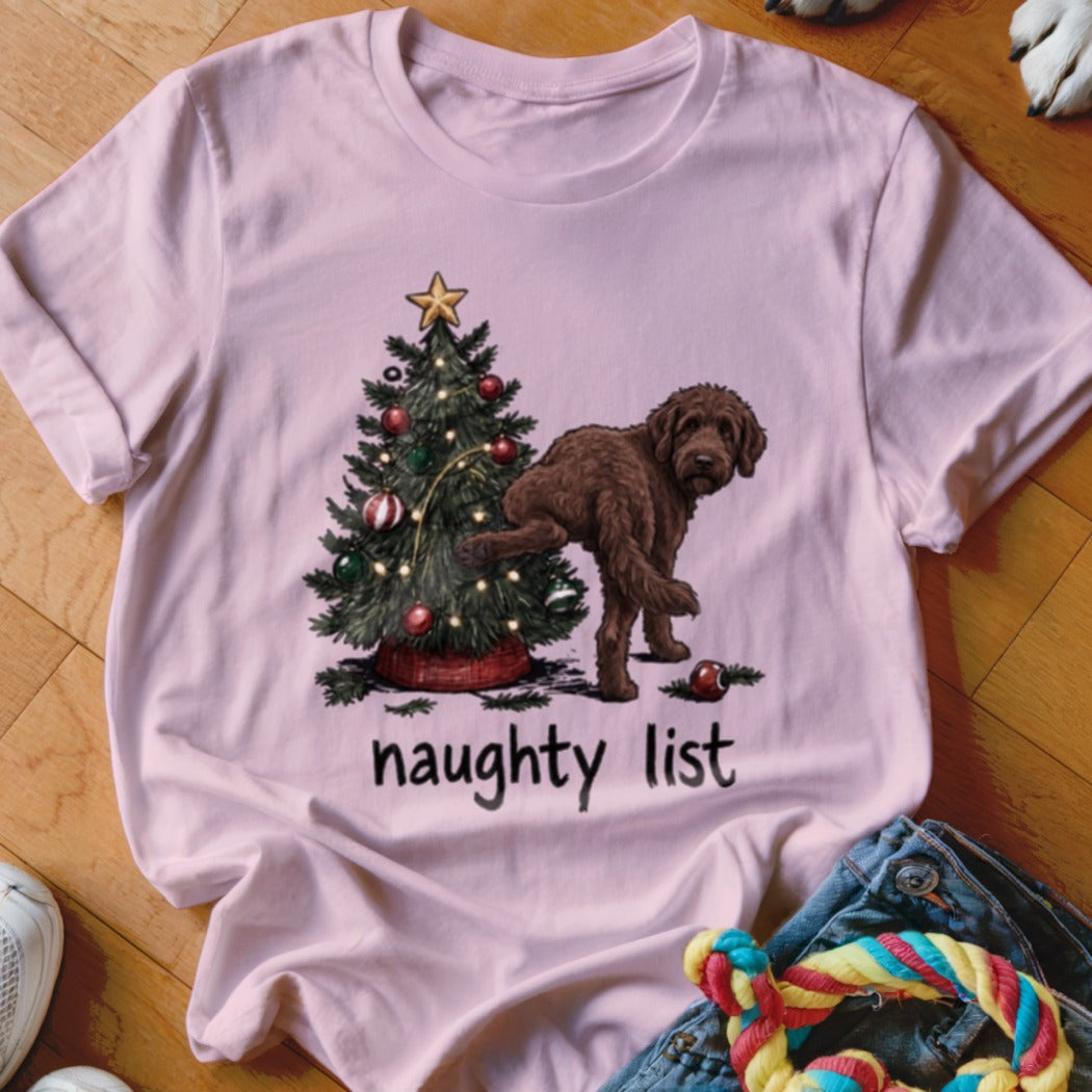 Pink t-shirt with a brown dog next to a Christmas tree, text says "naughty list".