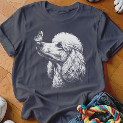 A dark grey t-shirt featuring a white sketch graphic of a standard poodle looking at a butterfly on its nose.