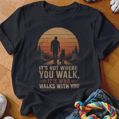 Black t-shirt with a person and dog walking at sunset. Text reads "IT'S NOT WHERE YOU WALK, IT'S WHO WALKS WITH YOU".