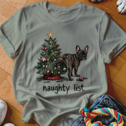 A sage green t-shirt featuring a graphic of a French bulldog peeing on a Christmas tree, with the text "naughty list".