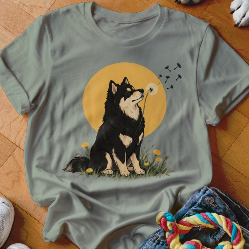 Sage green t-shirt featuring an illustration of a black dog blowing dandelion seeds against a yellow moon.