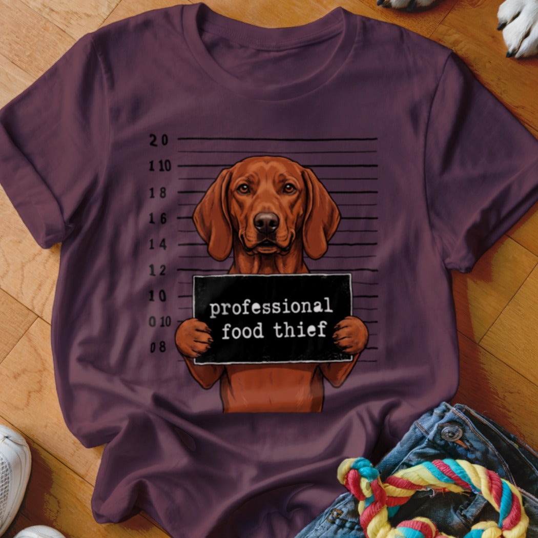 Brown dog mugshot with "professional food thief" sign on t-shirt.