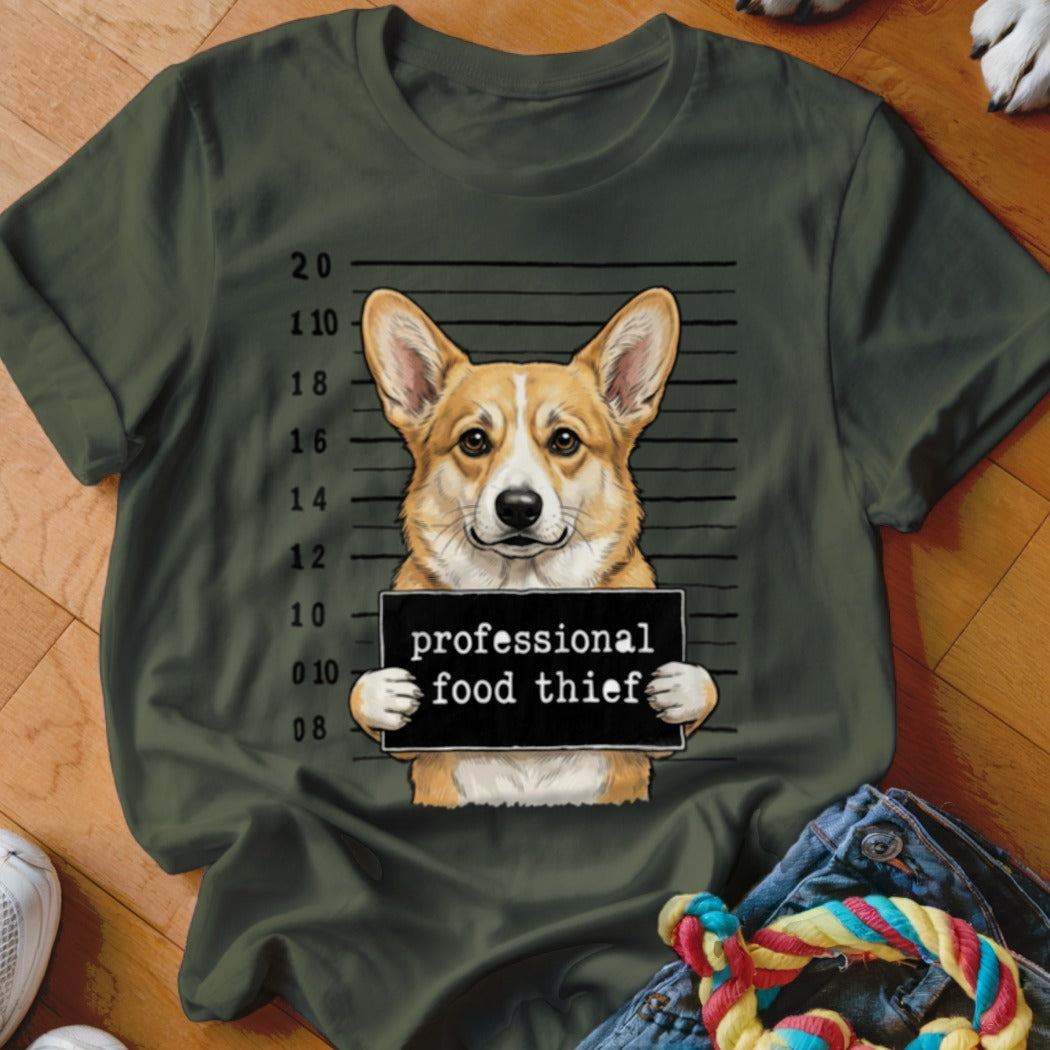 Corgi dog mugshot with "professional food thief" sign on a green t-shirt.