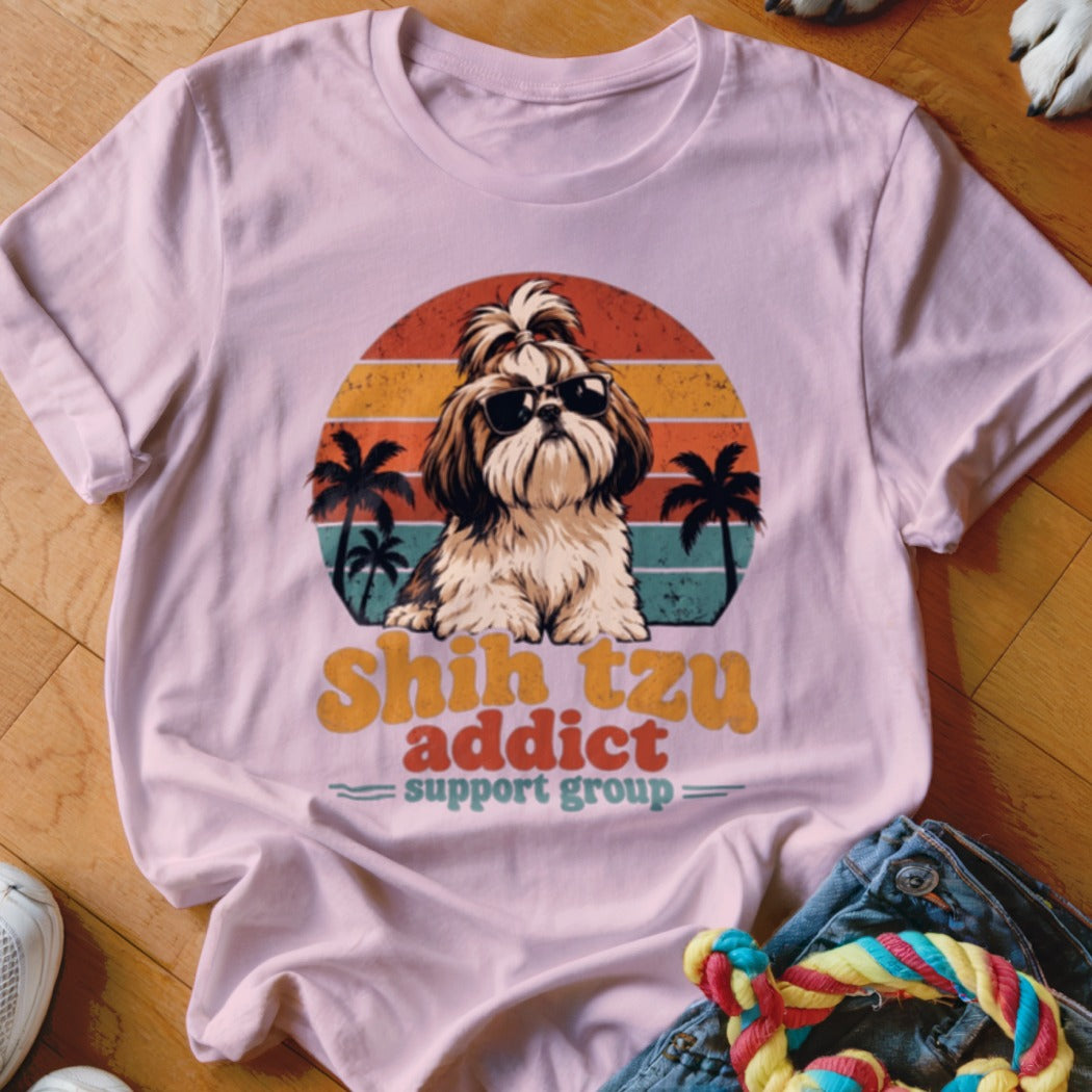 A light pink t-shirt with a vintage-style graphic of a Shih Tzu wearing sunglasses against a sunset and palm tree background.