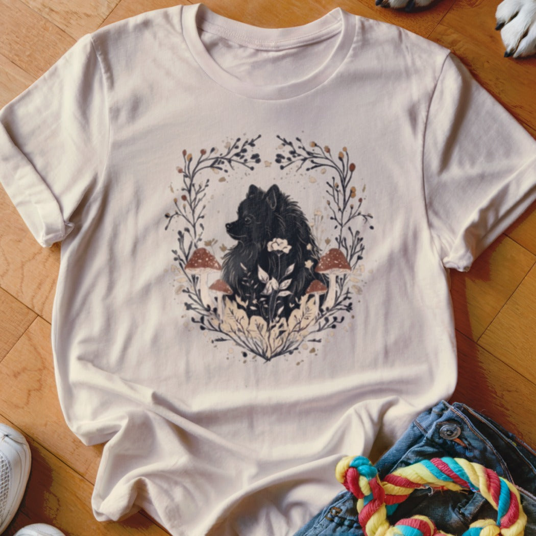 A cream-colored crewneck t-shirt featuring a black Pomeranian surrounded by mushrooms, leaves, and floral illustrations.