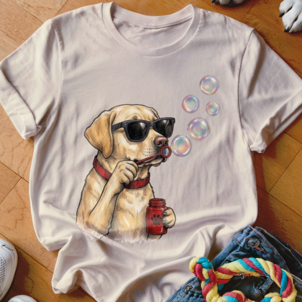 A cream-colored t-shirt features a graphic of a yellow Labrador wearing sunglasses and blowing bubbles.