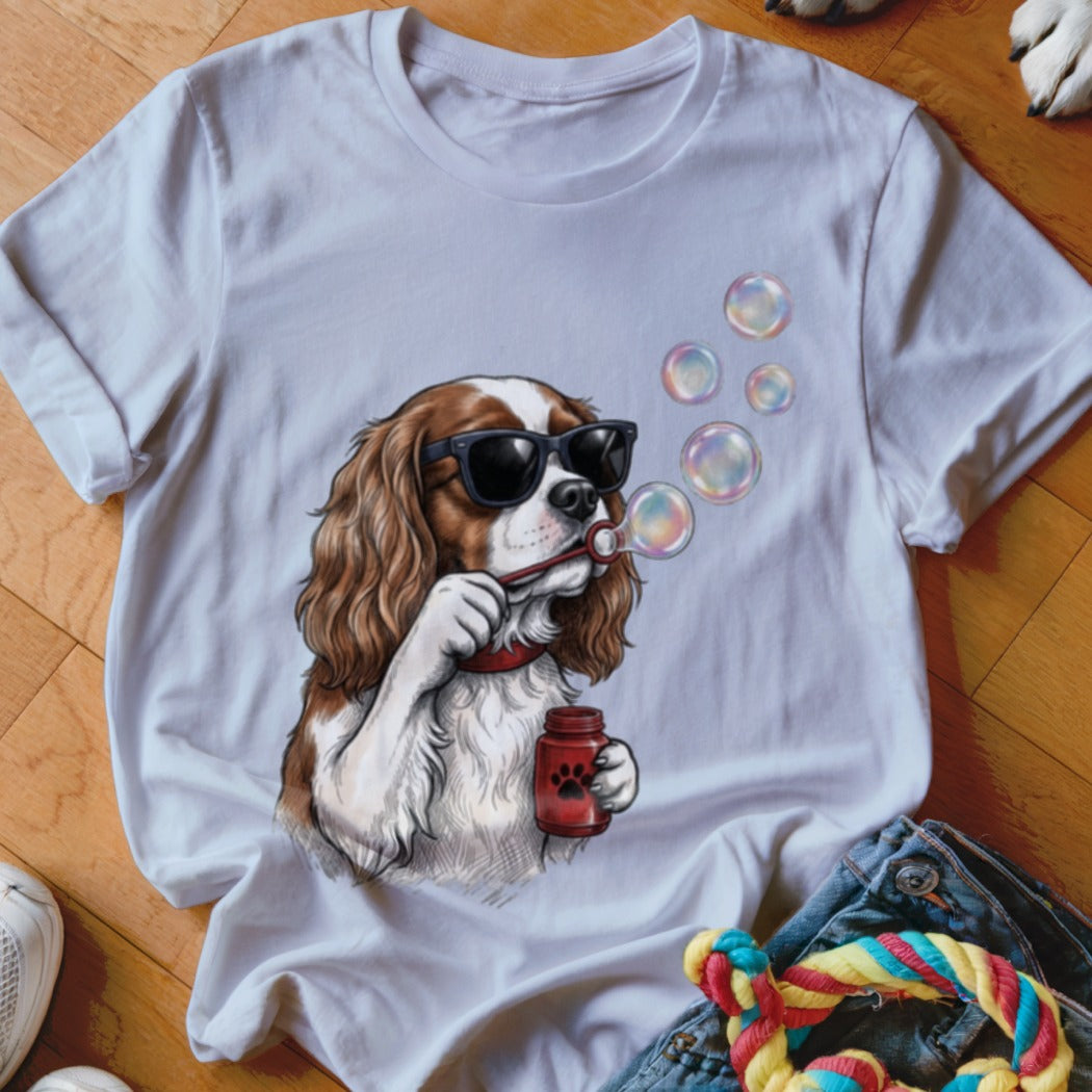 A white t-shirt featuring an illustration of a Cavalier King Charles Spaniel wearing sunglasses and blowing bubbles.