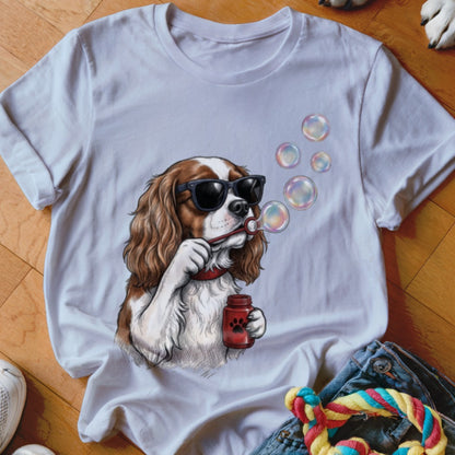 A white t-shirt featuring an illustration of a Cavalier King Charles Spaniel wearing sunglasses and blowing bubbles.