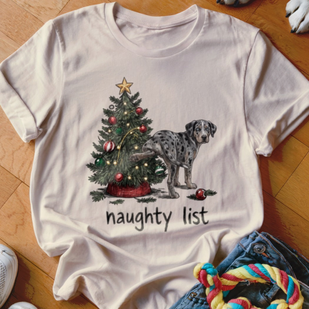 Beige t-shirt featuring a graphic of a spotted dog peeing on a Christmas tree with text reading naughty list.