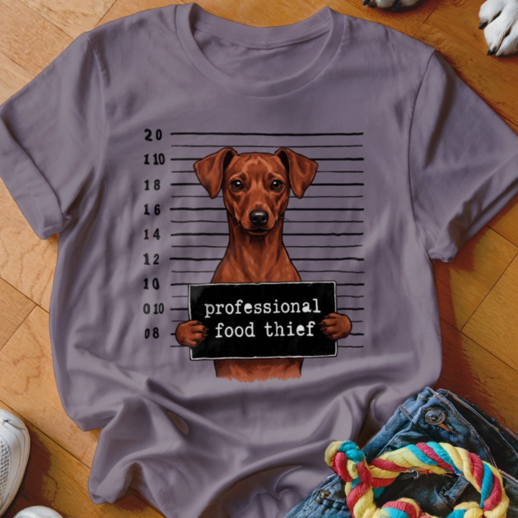 T-shirt graphic of a dog holding a "professional food thief" sign against a mugshot background.