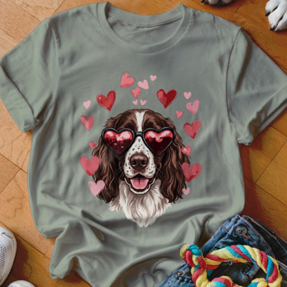 An olive green t-shirt featuring a graphic of a brown and white dog wearing heart-shaped sunglasses surrounded by pink hearts.