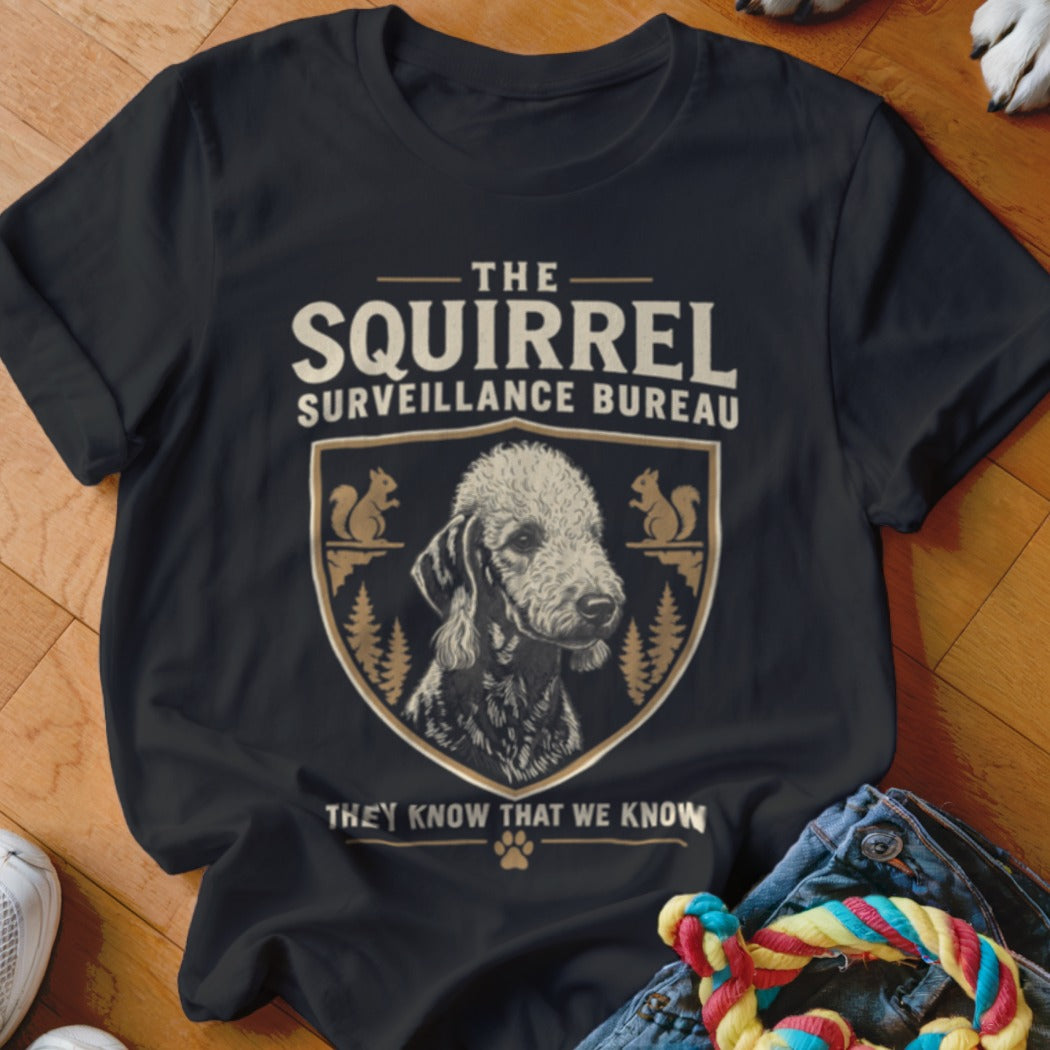 A black t-shirt printed with a dog crest and text reading The Squirrel Surveillance Bureau.