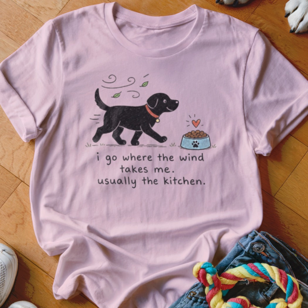 Pink t-shirt with illustration of a black dog and text "i go where the wind takes me. usually the kitchen."