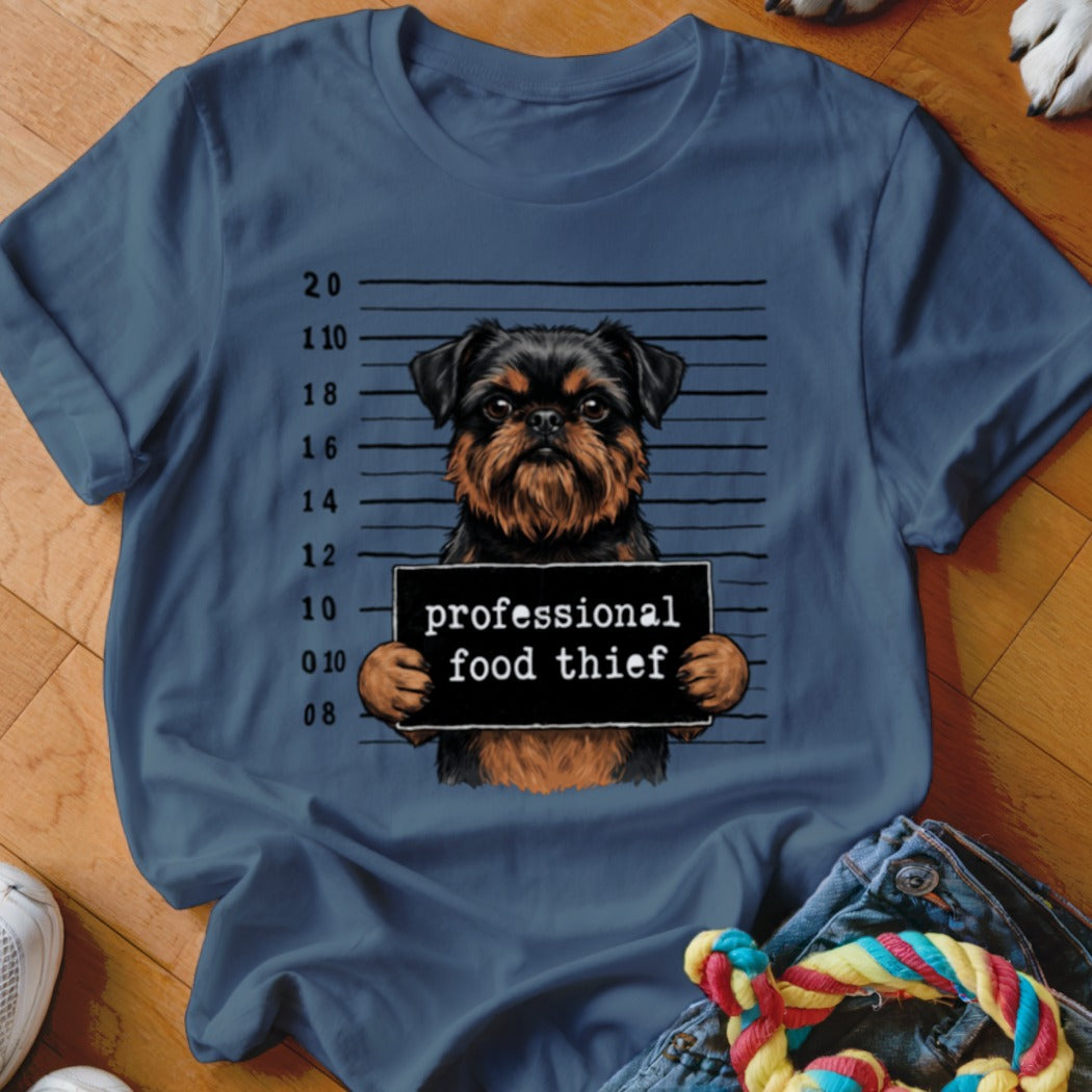 Brusssels Griffon dog mugshot with "professional food thief" sign on t-shirt.