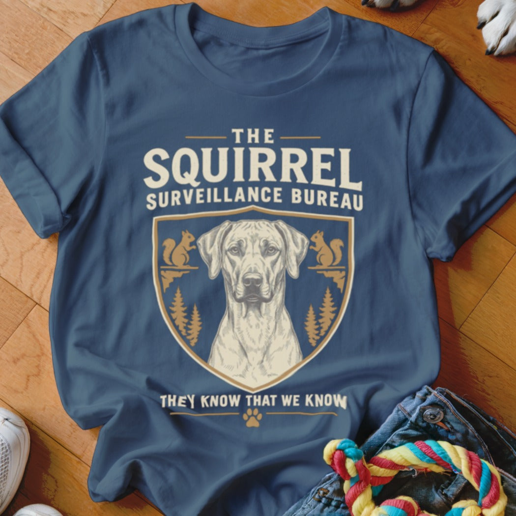 A dark blue t-shirt printed with a crest featuring a dog, squirrels, and the text The Squirrel Surveillance Bureau.
