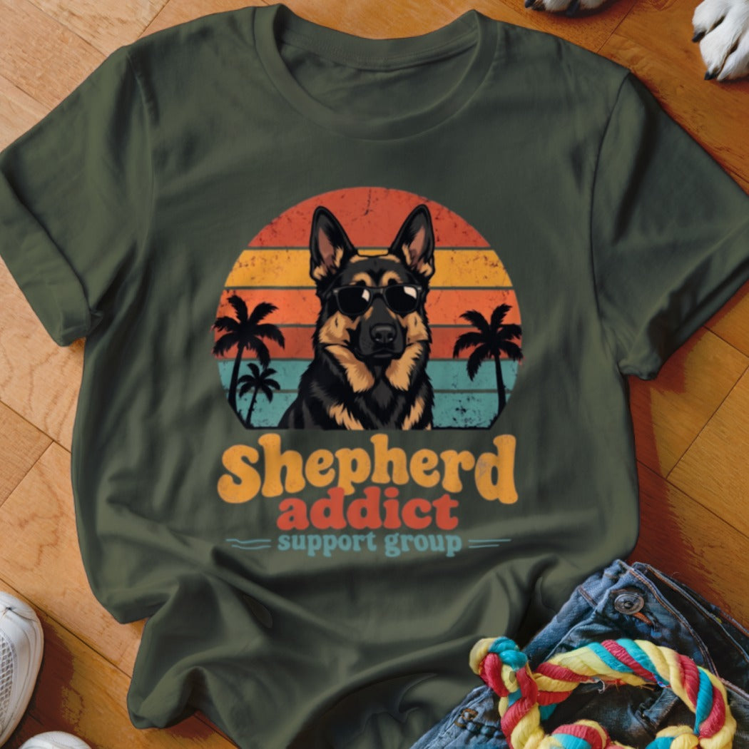 Dark green t-shirt featuring a German Shepherd wearing sunglasses in front of a retro sunset graphic with palm trees and the text "Shepherd addict support group".