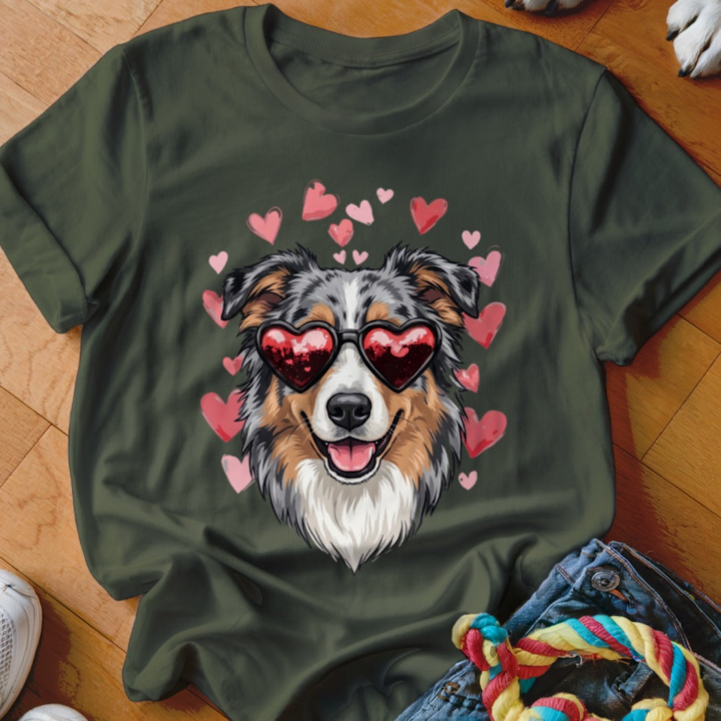 An olive green t-shirt featuring an illustration of an Australian Shepherd wearing heart-shaped sunglasses, surrounded by pink hearts.