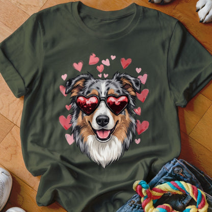 An olive green t-shirt featuring an illustration of an Australian Shepherd wearing heart-shaped sunglasses, surrounded by pink hearts.