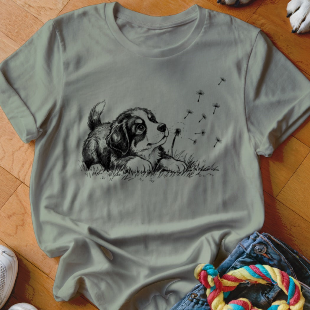 Sage green crewneck t-shirt featuring a black-and-white sketch of a puppy watching floating dandelion seeds.