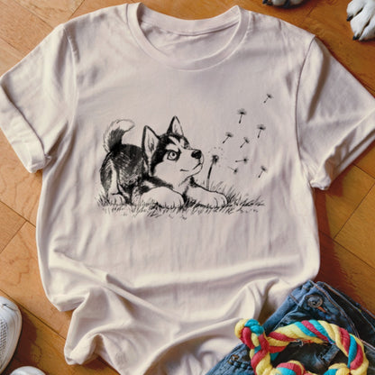 A cream-colored t-shirt with a black line drawing of a husky puppy playing with dandelion seeds.