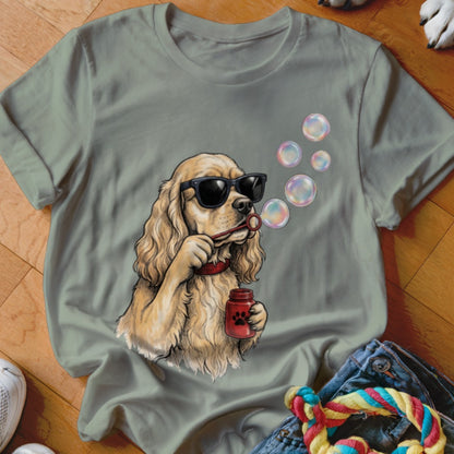 A gray t-shirt featuring a graphic of a golden spaniel wearing sunglasses and blowing soap bubbles.