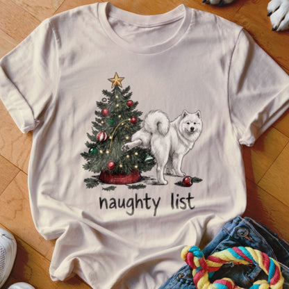 A light-colored t-shirt featuring a graphic of a white dog peeing on a Christmas tree with the text naughty list.