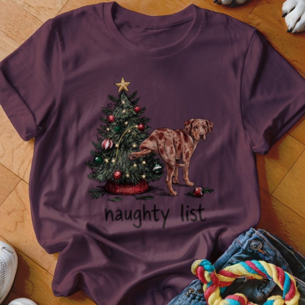 A maroon t-shirt with a graphic of a spotted dog peeing on a Christmas tree above the text "naughty list".