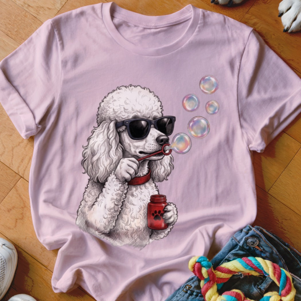 A light pink t-shirt features a graphic of a white poodle wearing sunglasses and blowing soap bubbles.
