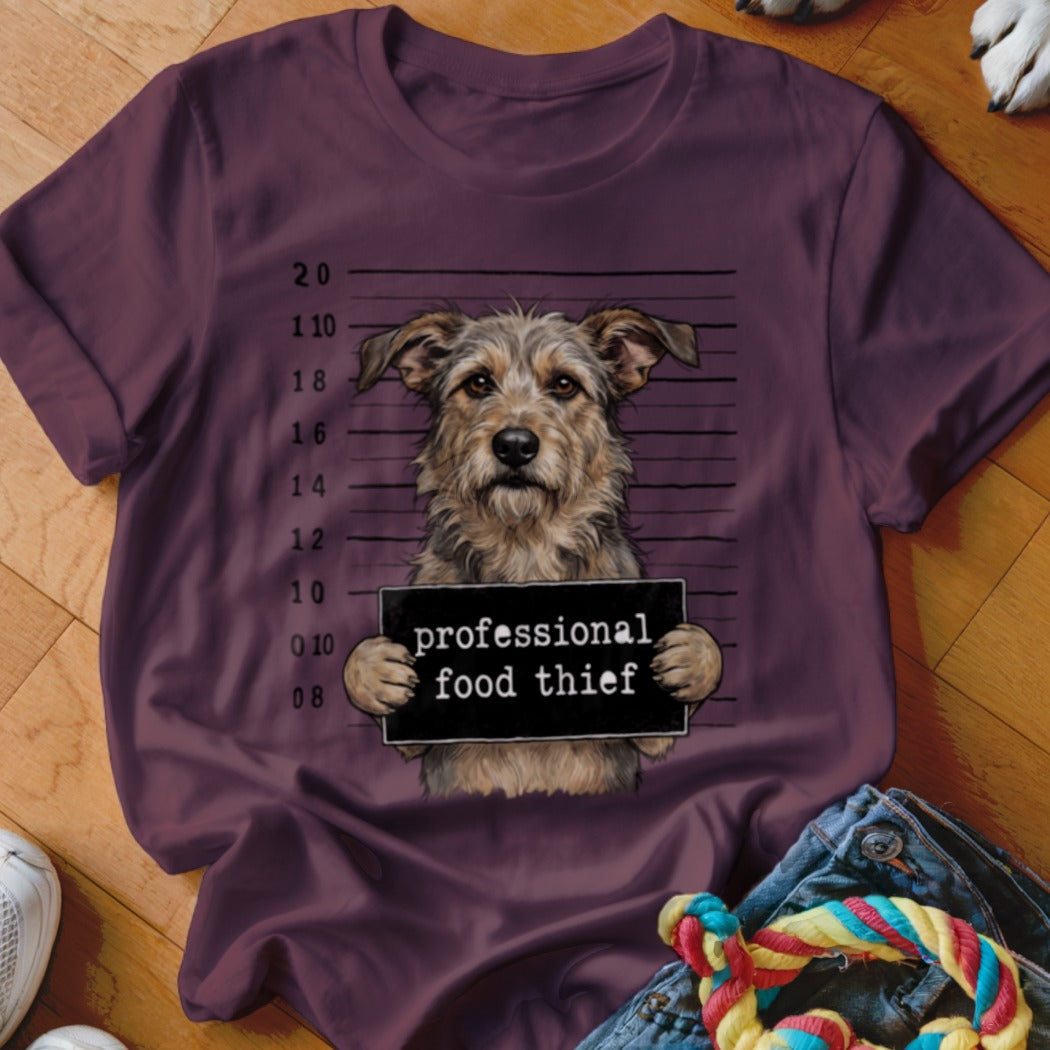 A terrier mix dog holds a sign that reads "professional food thief".